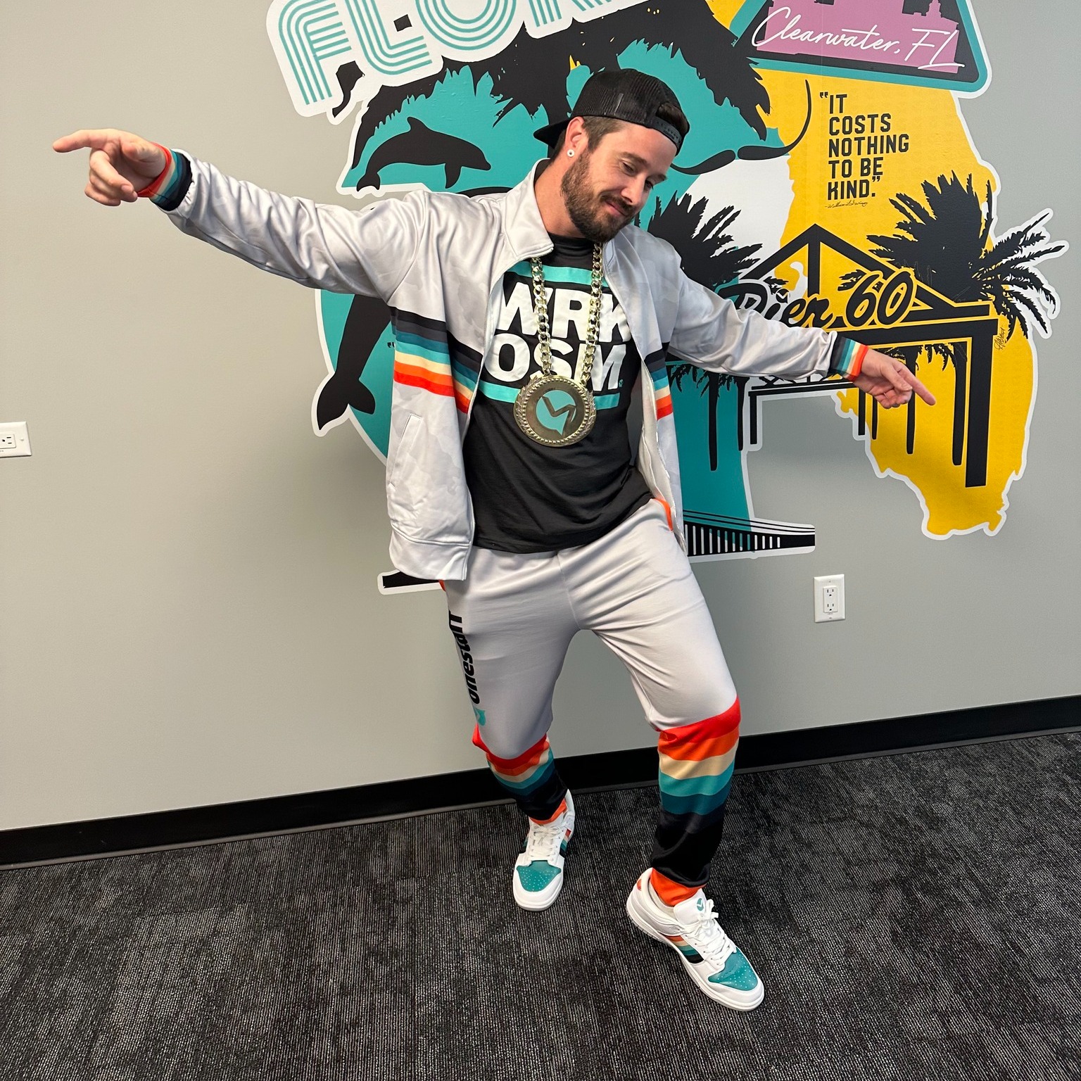 OneStaff team member in the full retro hip hop kit — track jacket, champ chain, snapback, and custom track pants in front of the activation backdrop