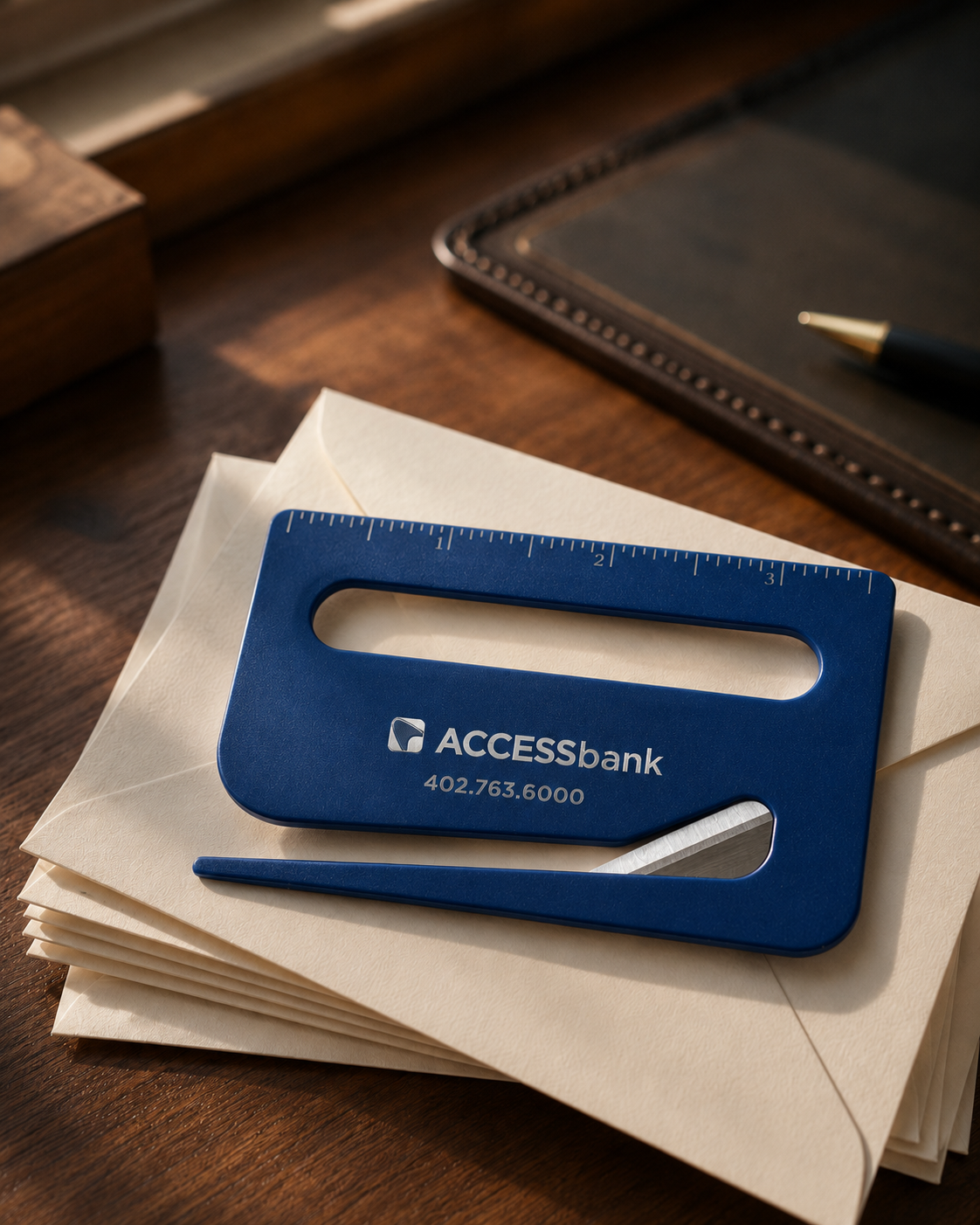 ACCESSbank branded envelope opener with a silver metallic ink overlay, resting on a stack of envelopes