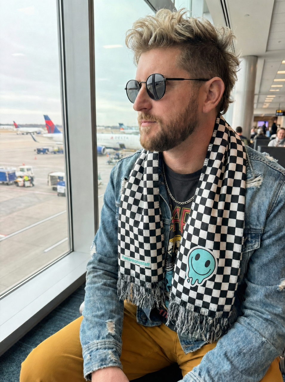 Travel nurse in an airport terminal wearing the OneStaff checkered scarf with smiley graphic, en route to the next assignment